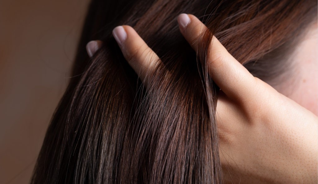 Eine Frauenhand greift sich ins volle lange Haare. Eine Haardiagnostik findet die Ursachen für Haarausfall.